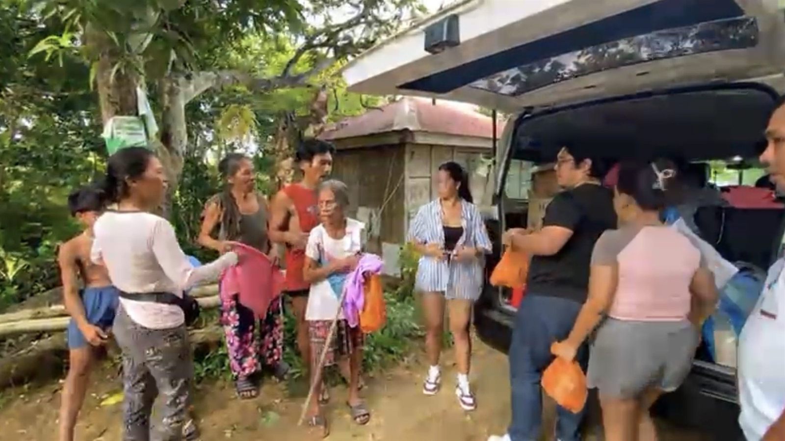 Volunteers passing orange bags from the back of a van to residents, an older woman with a walking stick waiting her turn