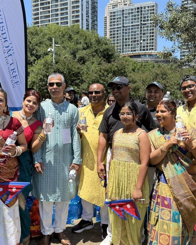 Festival-goers in saris and kurtas holding bottled water, Nepali flags in their hands